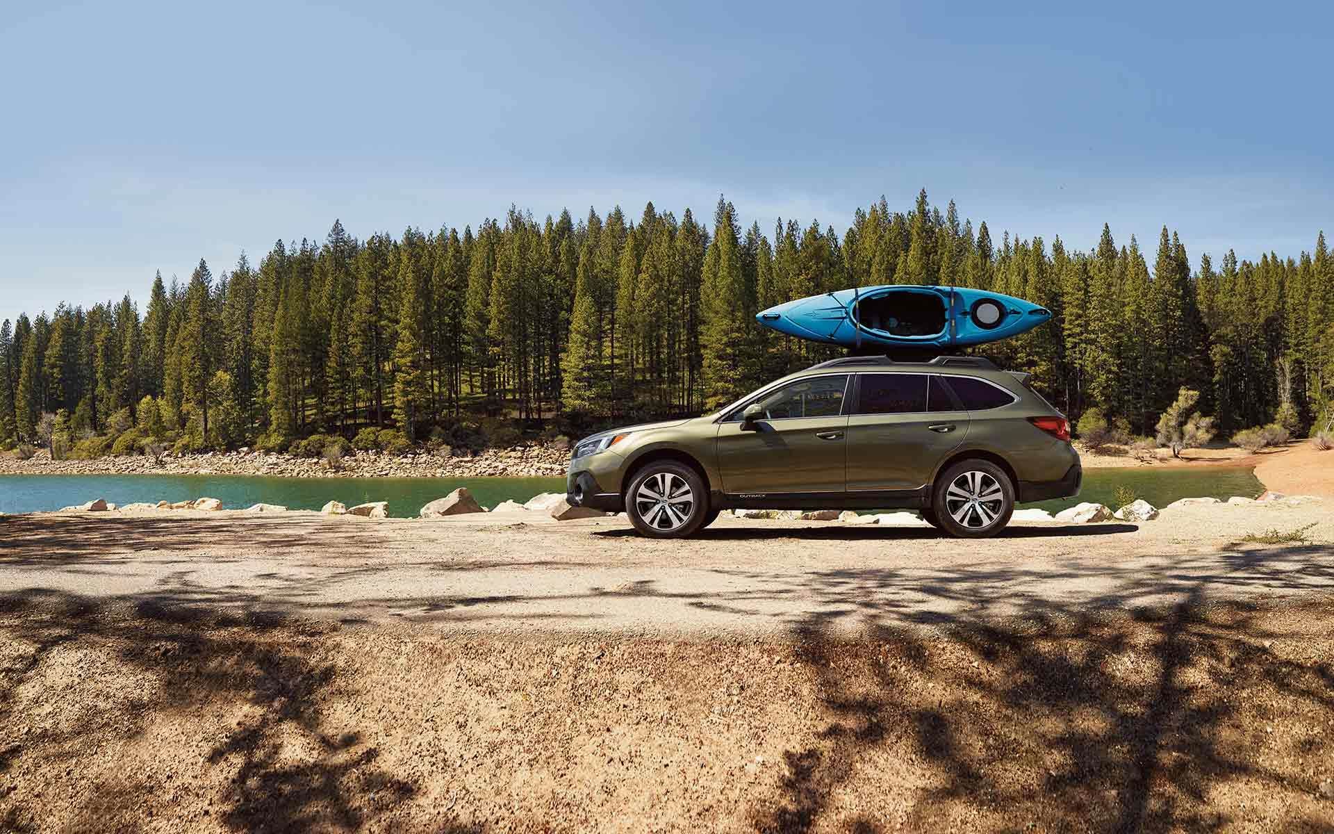 Subaru Outback with a kayak on the roof parked in front of trees