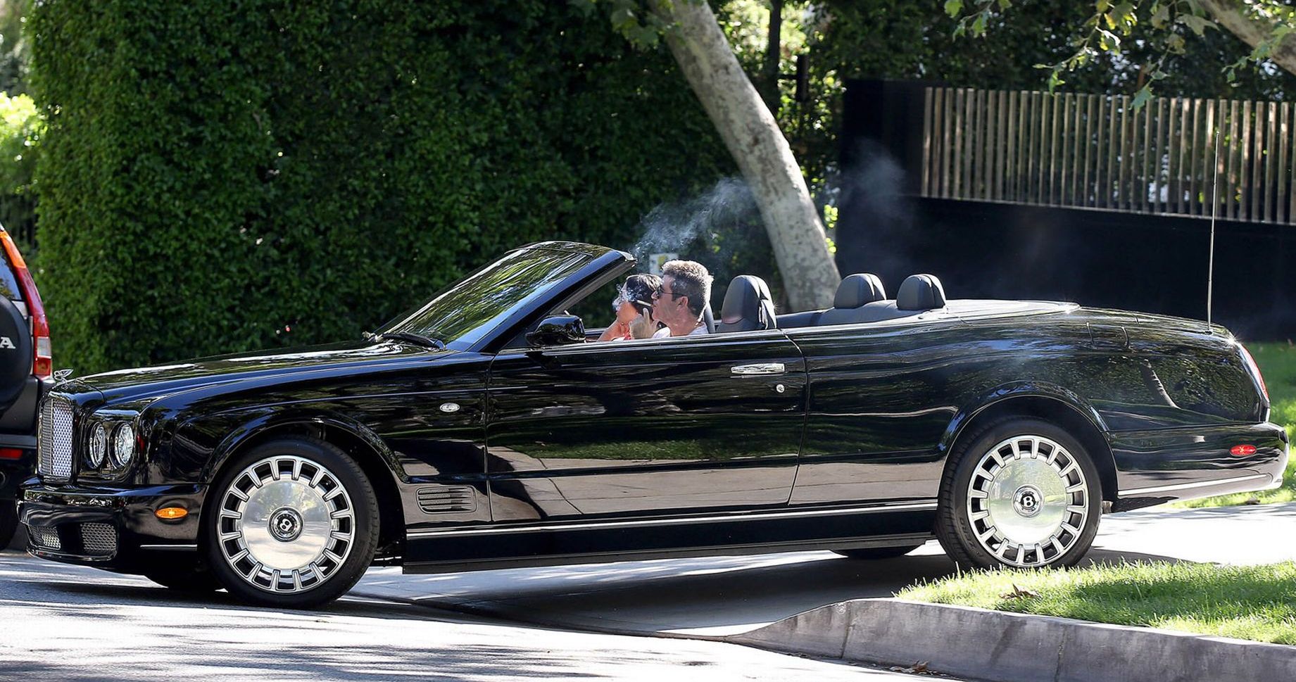 Simon Cowell smoking in his black Bentley Azure