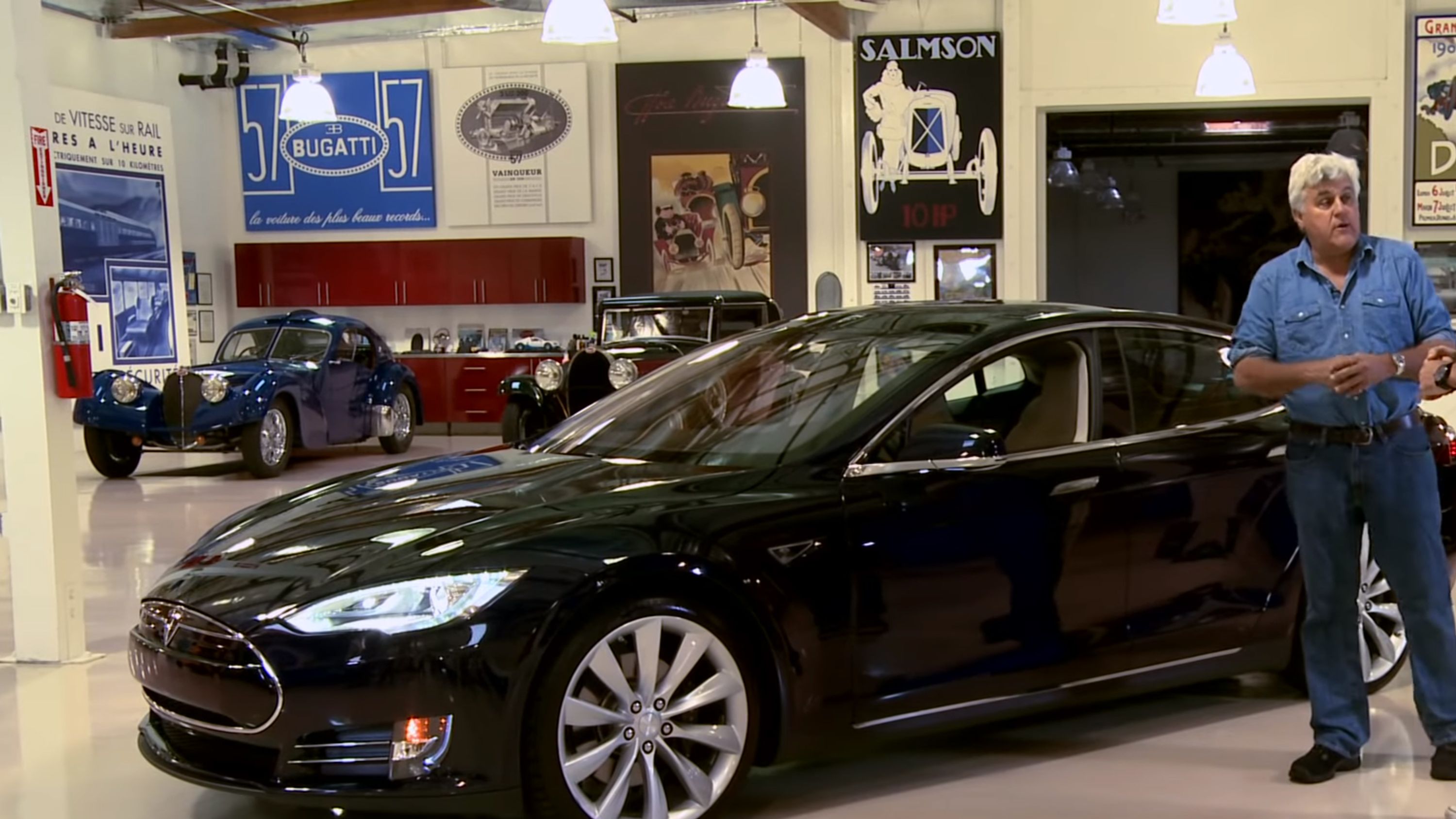 Jay Leno stands next to a black Tesla Model S