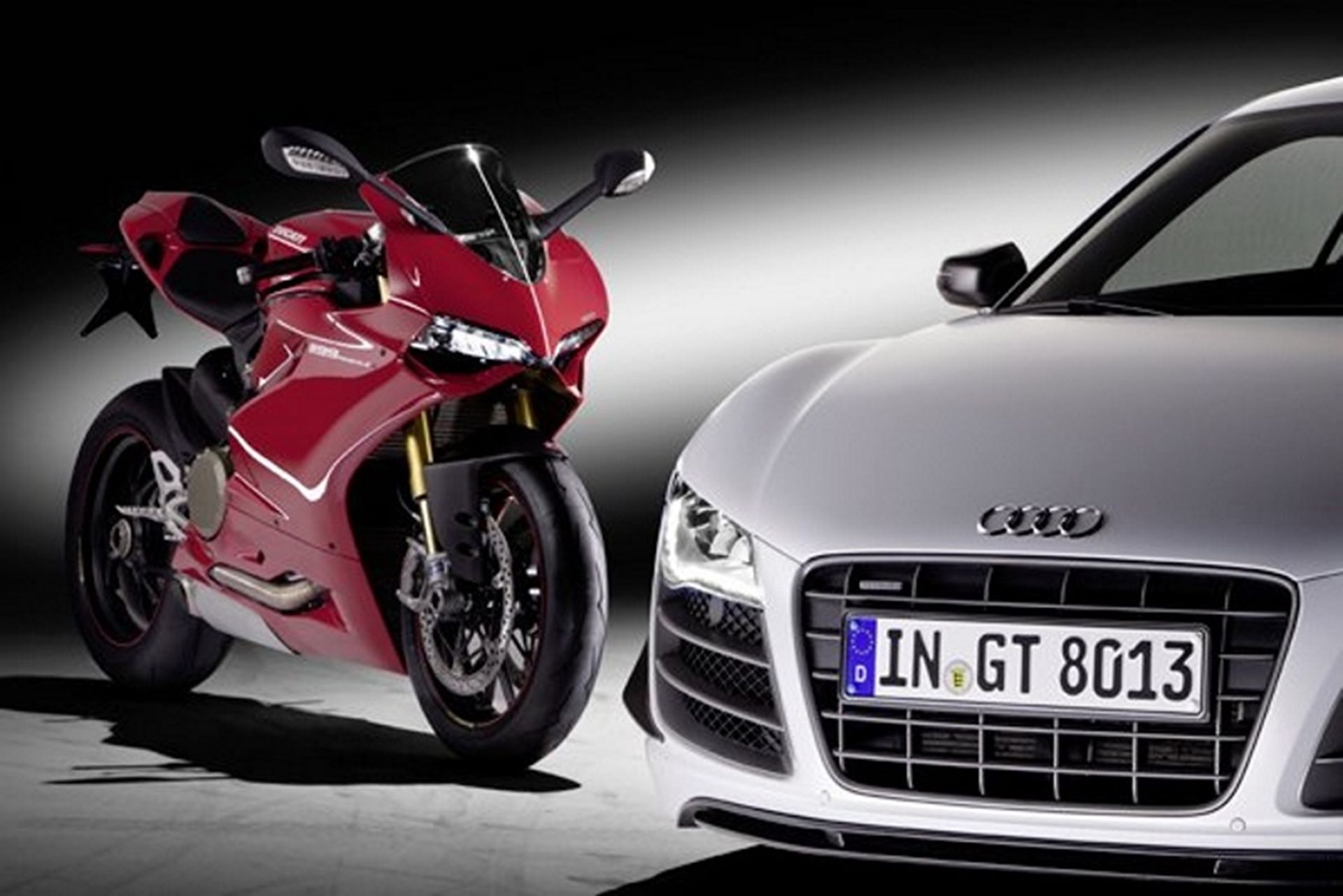 red Ducati motorcycle behind the front end of a silver Audi R8