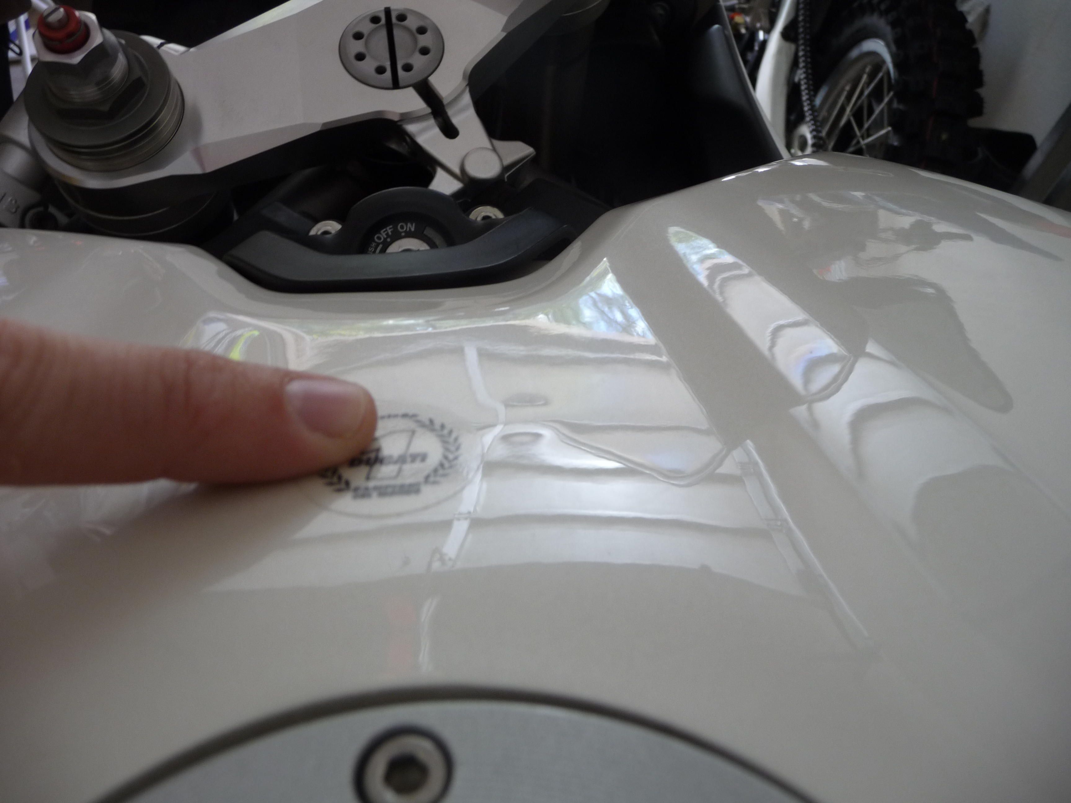 Finger points at a deformity on a white Ducati fuel tank