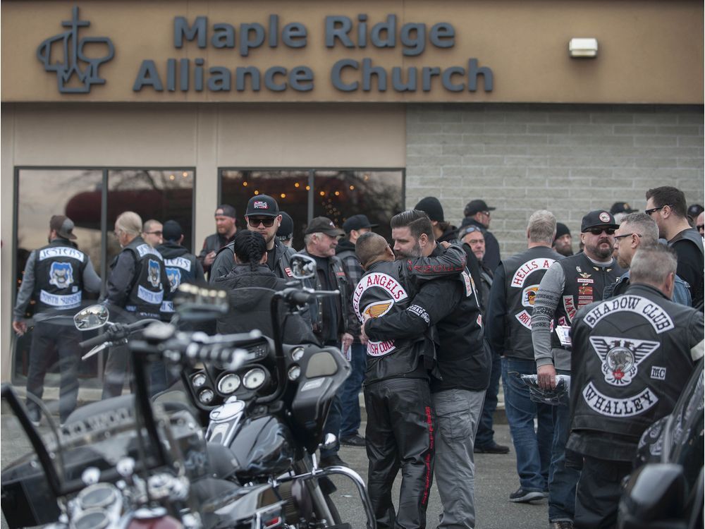 Riders, tears, and consoling embraces accumulate outside the church service for a fallen member.