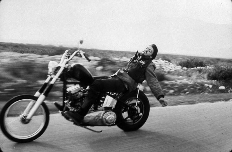 A risky Hell's Angel rider playfully leans back on his bike down a California highway.