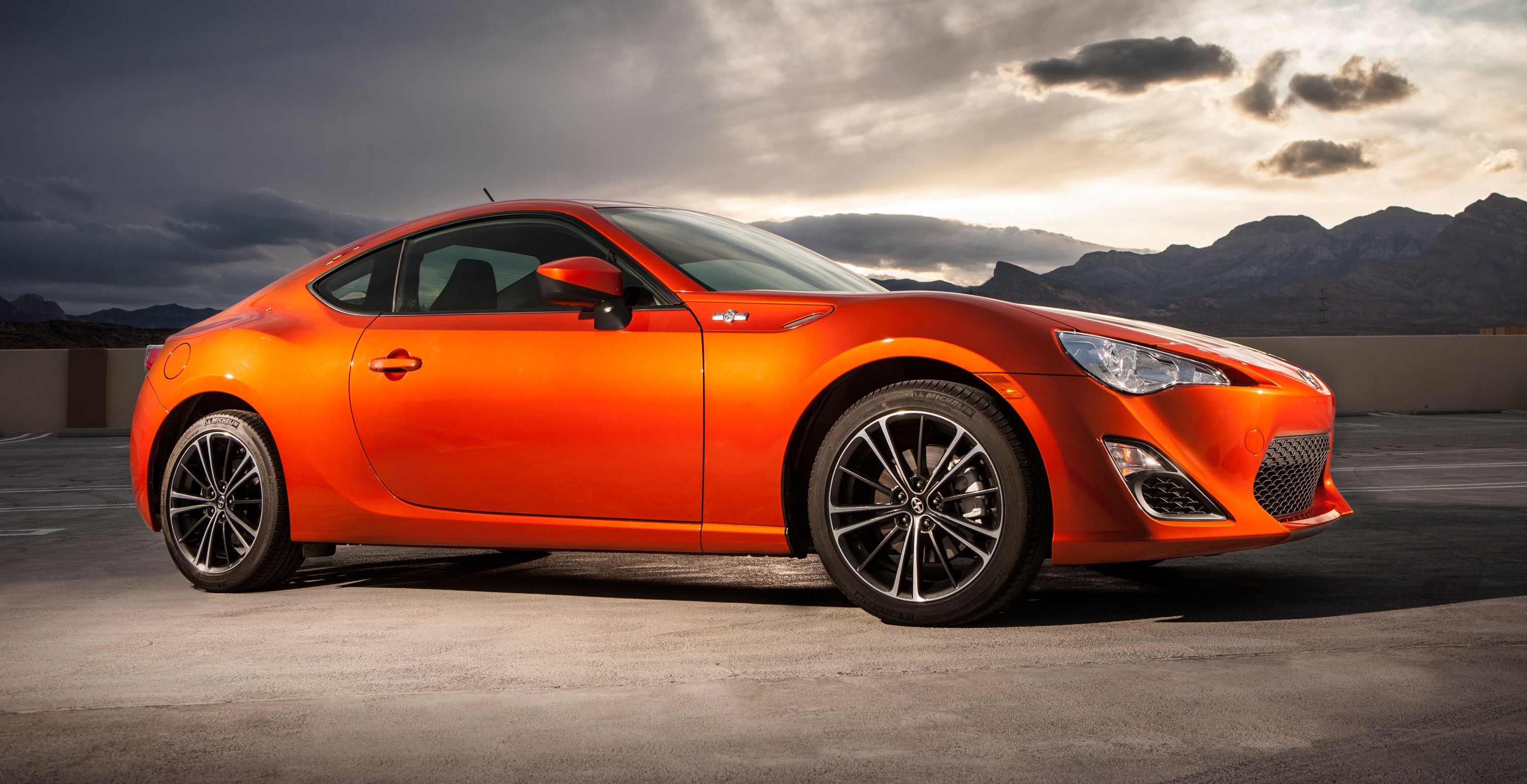 A 2013 Scion FR-S parked in front the sun setting behind mountains