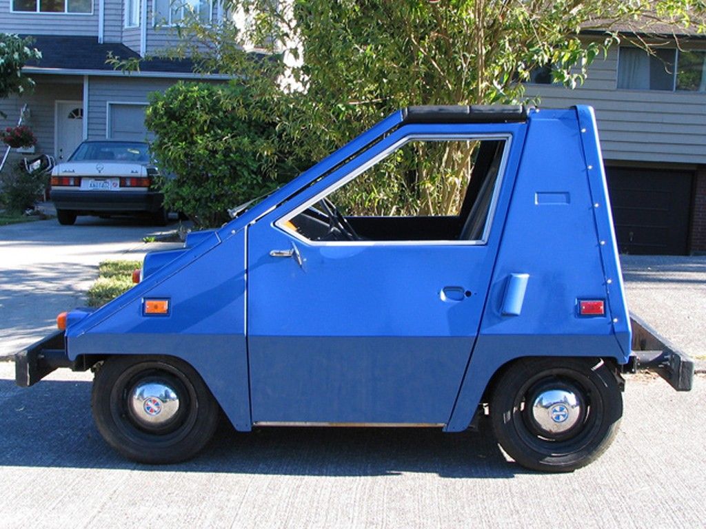 side view of a blue 1974 Sebring-Vanguard CitiCar on the street in front of a house