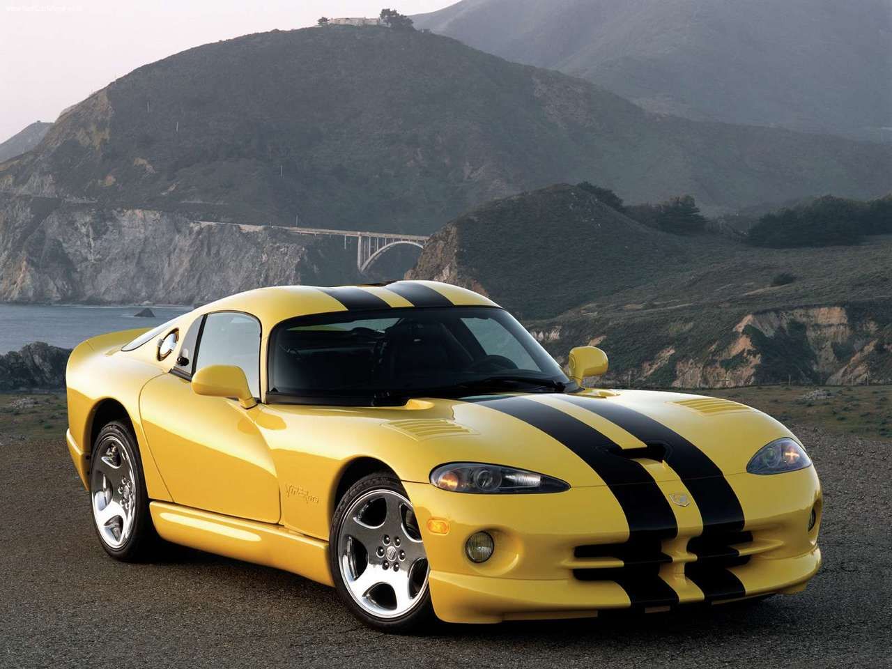 Bright Yellow 2001 Dodge Viper GTS with black stripes with a scenic landscape on the background