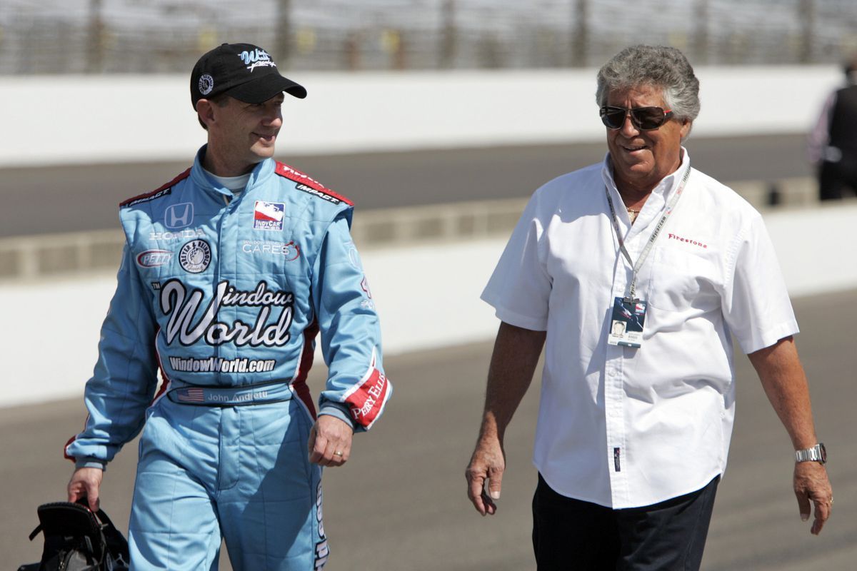 Mario Andretti standing next to guy in blue suit