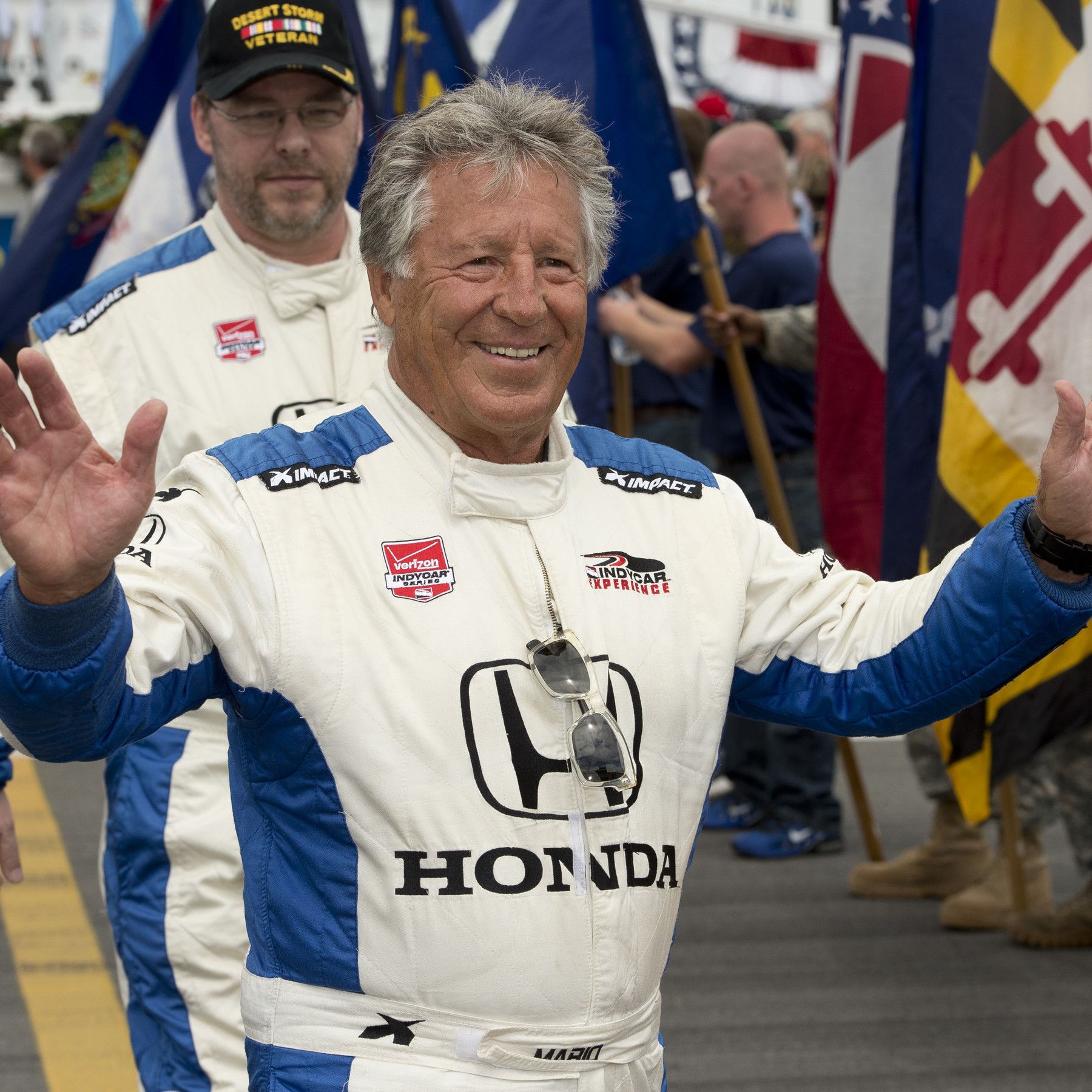 Mario Andretti in mostly white motorsuit looking happy