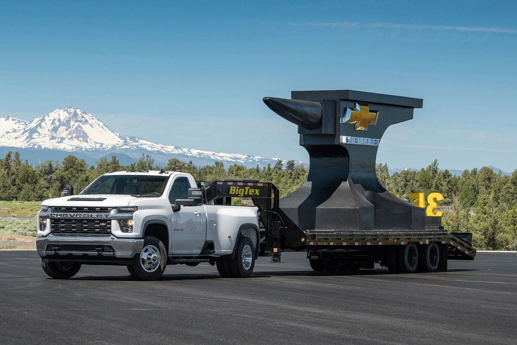 White Chevrolet Silverado towing a trailer bearing a massive anvil