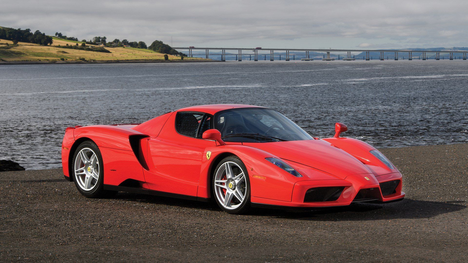 Red Enzo Ferrari parked on the tarmac next to a river