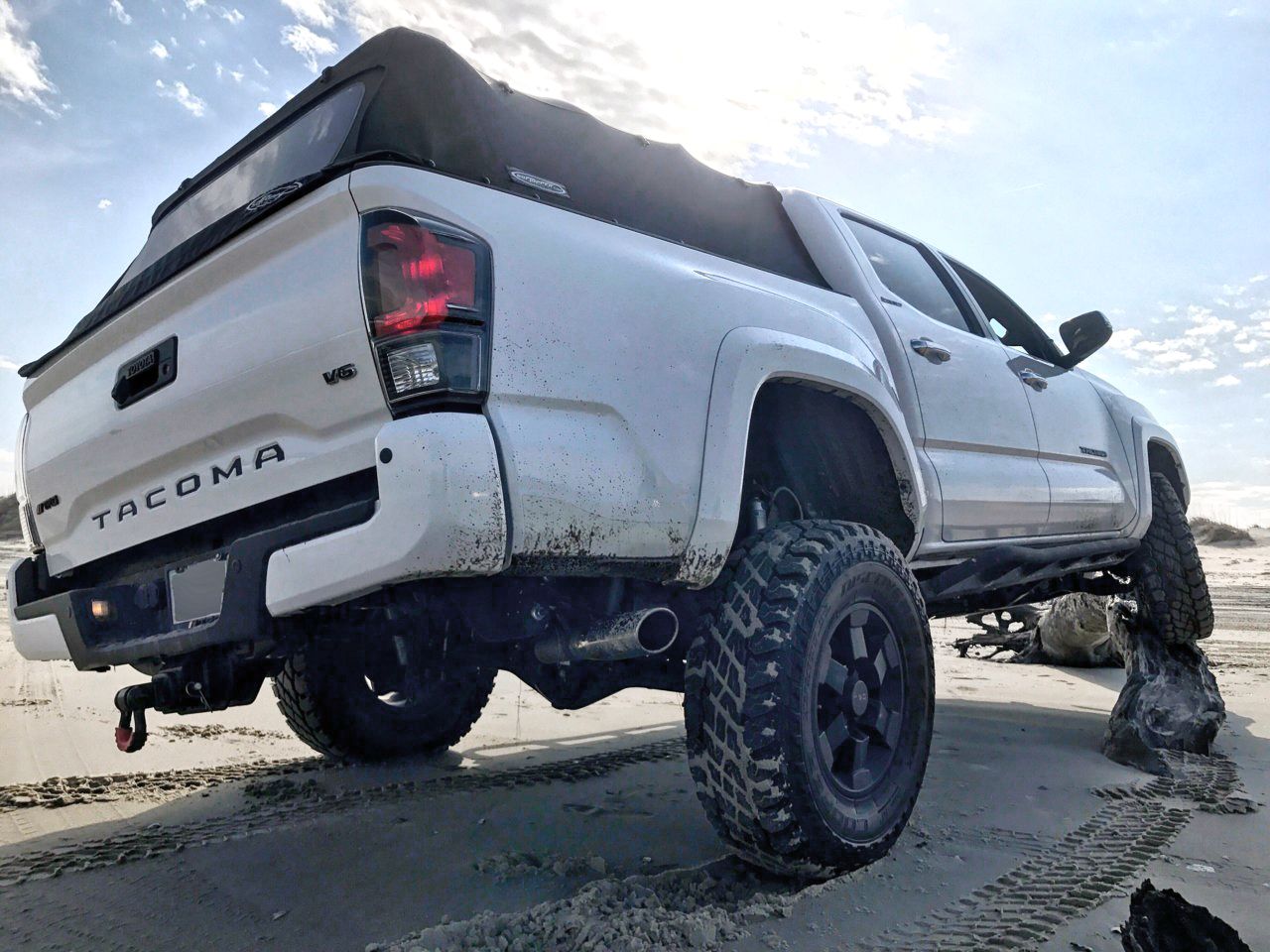3/4 rear view of a white Toyota Tacoma on the mud 