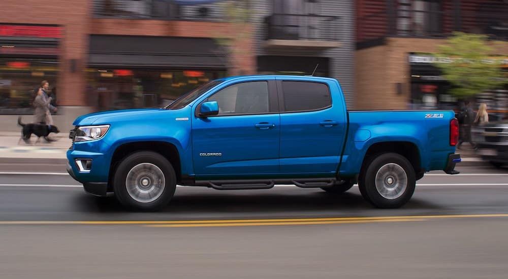 Side view of a metallic blue Chevrolet Colorado cruising an urban street 