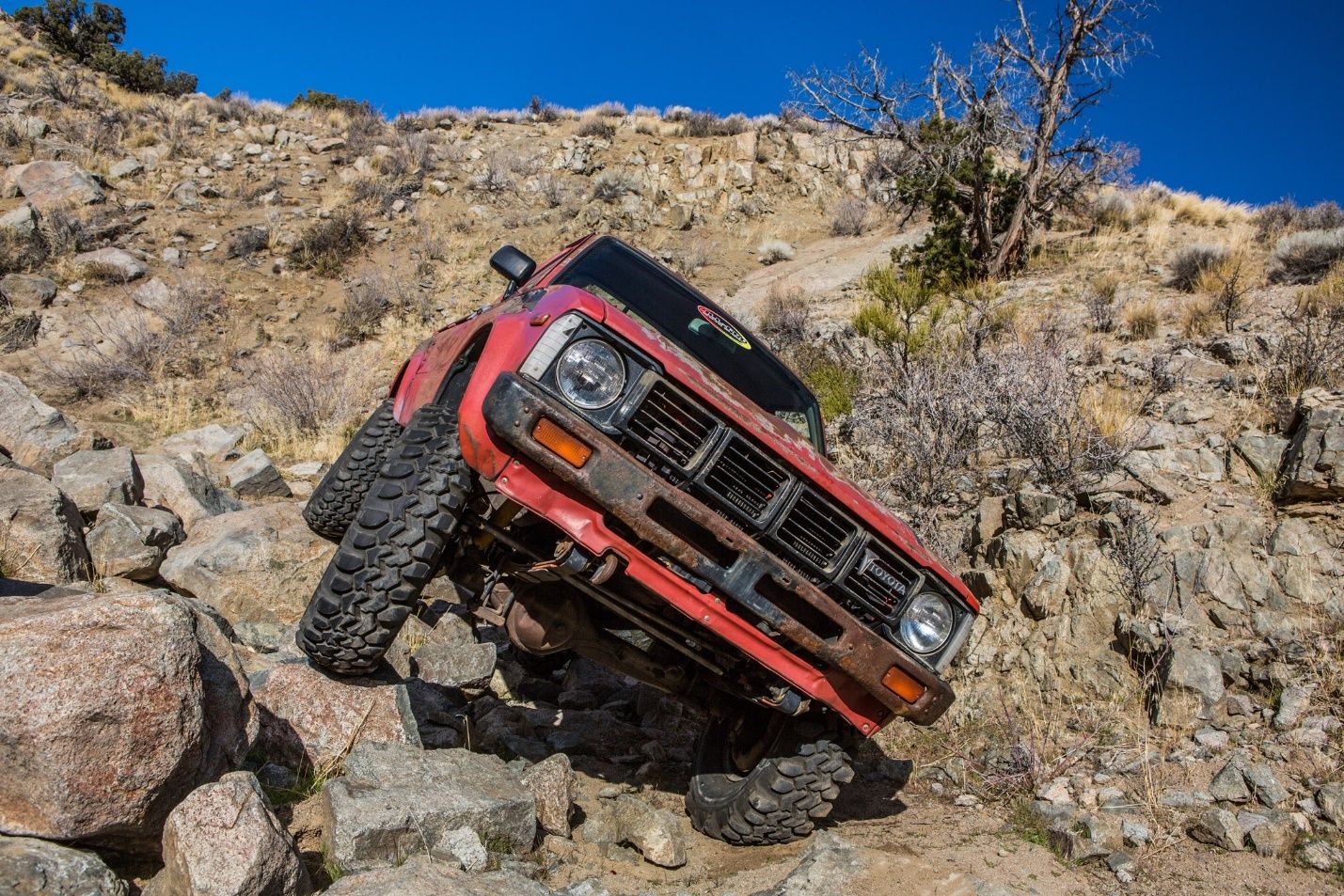 Red old Toyota Hilux going down a rocky hill 