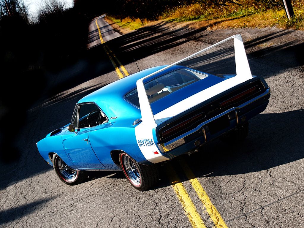3/4 rear view of a glorious bright blue poly 1969 Dodge Charger Daytona in the middle of a tarmac road