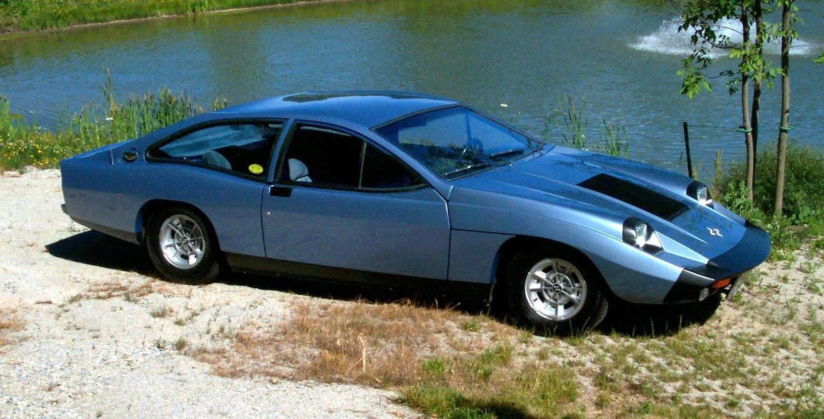Metallic blue Marcos Mantis parked on dirt by a pond