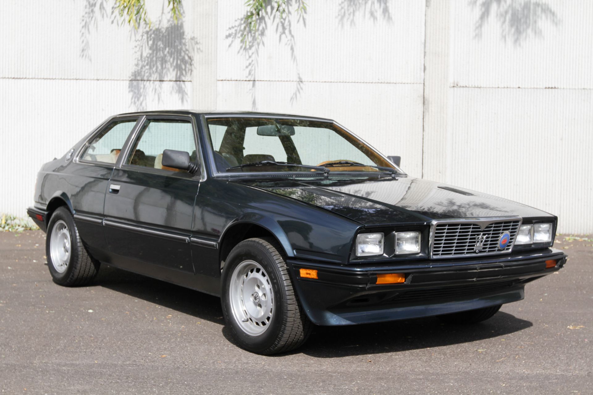 3/4 front view of a Dark Aquamarine Metallic Maserati BiTurbo in front of a white wall