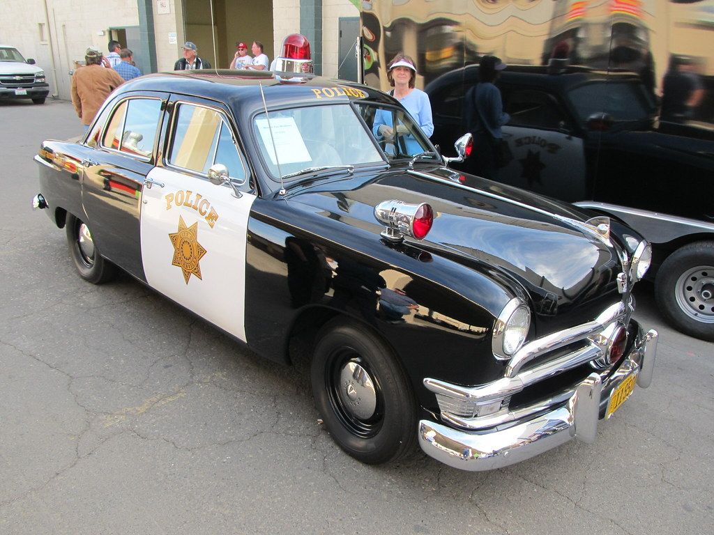 A lady stands next to a 50s era Ford police car