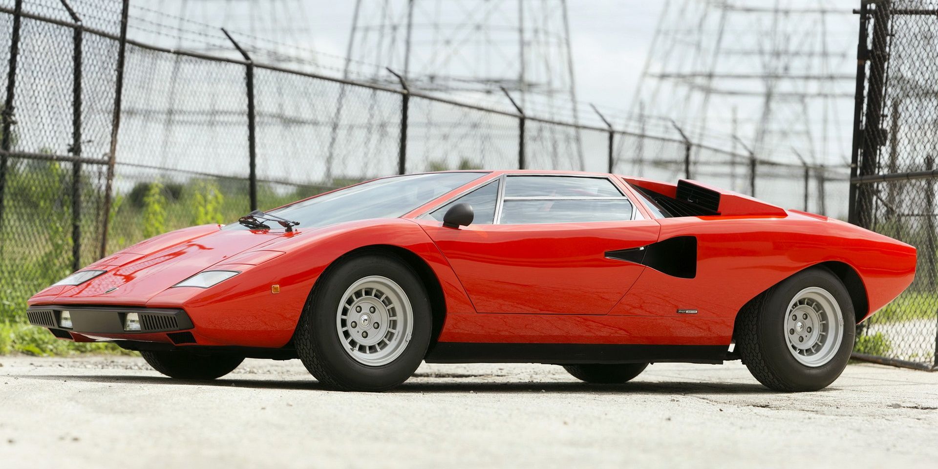 A red 1974 Lamborghini Countach Parked in front of a high-fenced ground