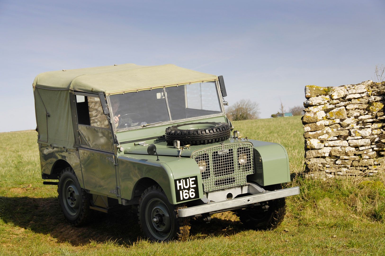 Military green Land Rover Series I driving on a green hill