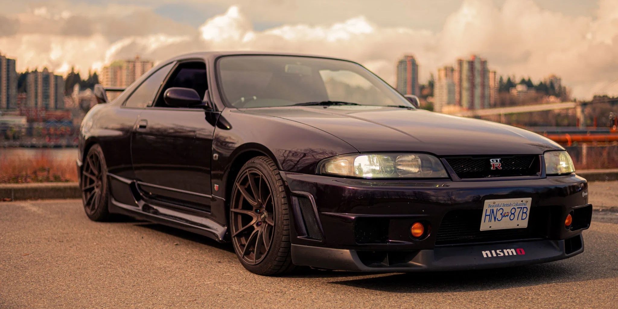 A black 1993 Nissan Skyline GTR R33 pictured against a city backdrop