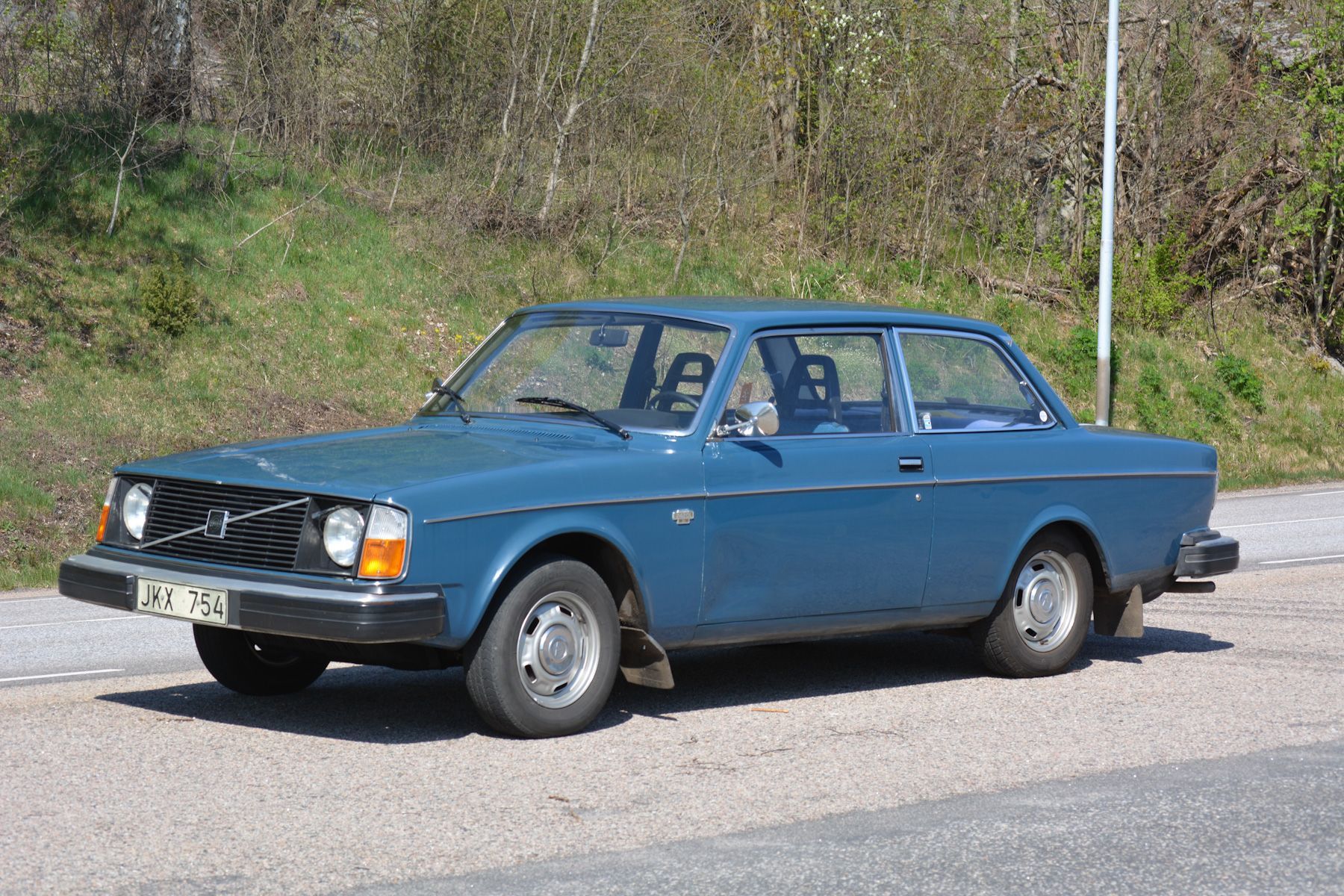 blue Volvo 142 outside by grassy hill