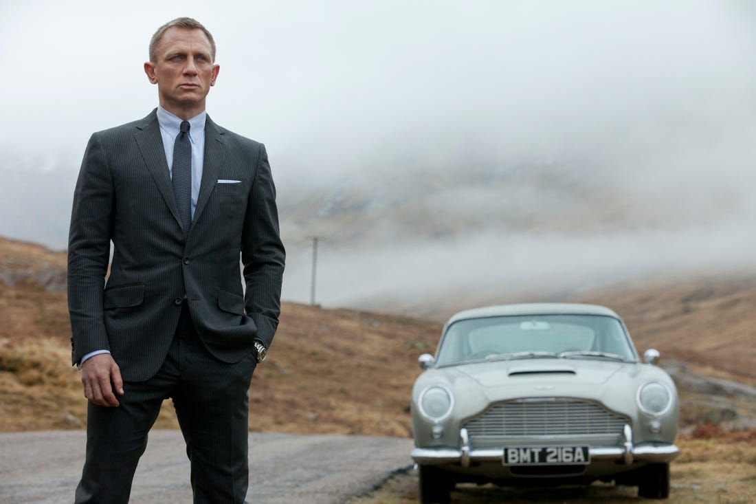 Danial Craig stands in front of the Aston Martin DB5