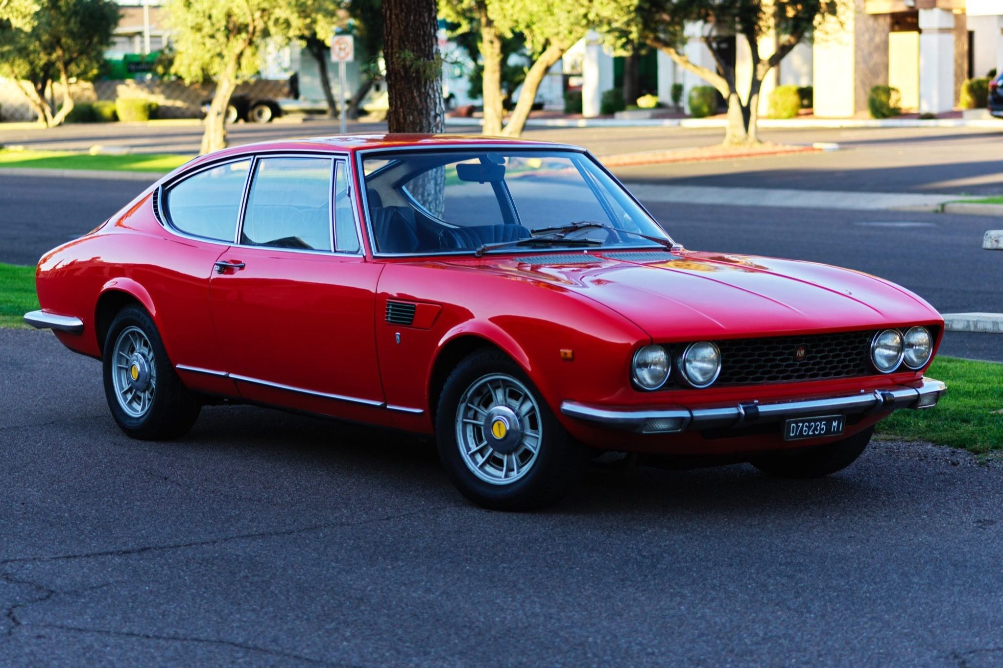 A 1967 red Fiat Dino stands parallel parked on a road.