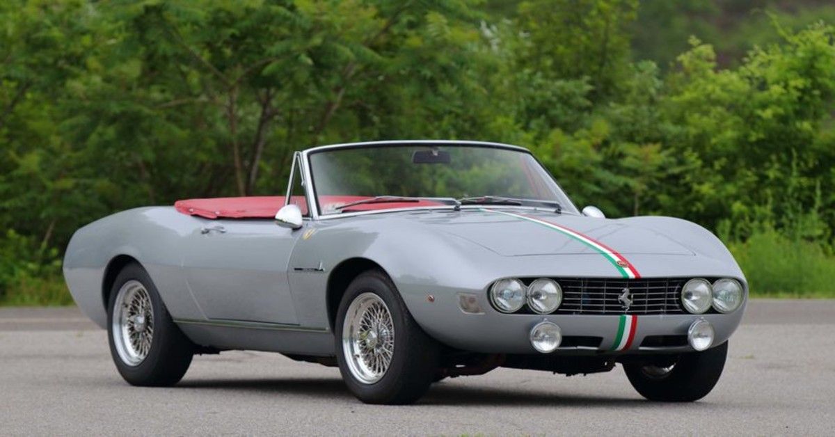 A grey 1967 Fiat Dino Spyder with stripes that feature the colors of the Italian flag stands parked on a road.