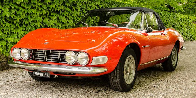 A red 1968 Fiat Dino stands parked in a backyard.