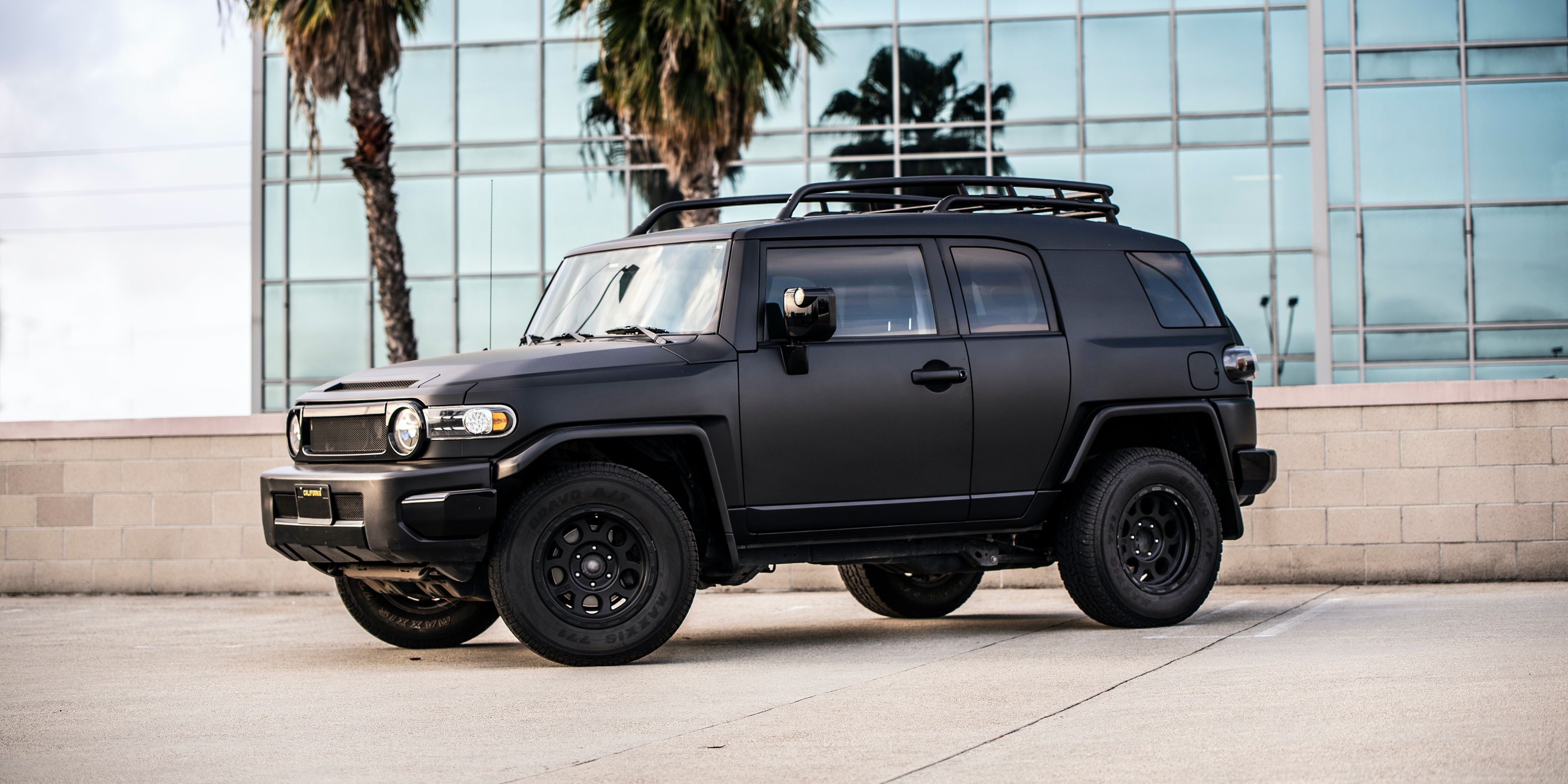 Black Toyota FJ Cruiser from side in front of glass building