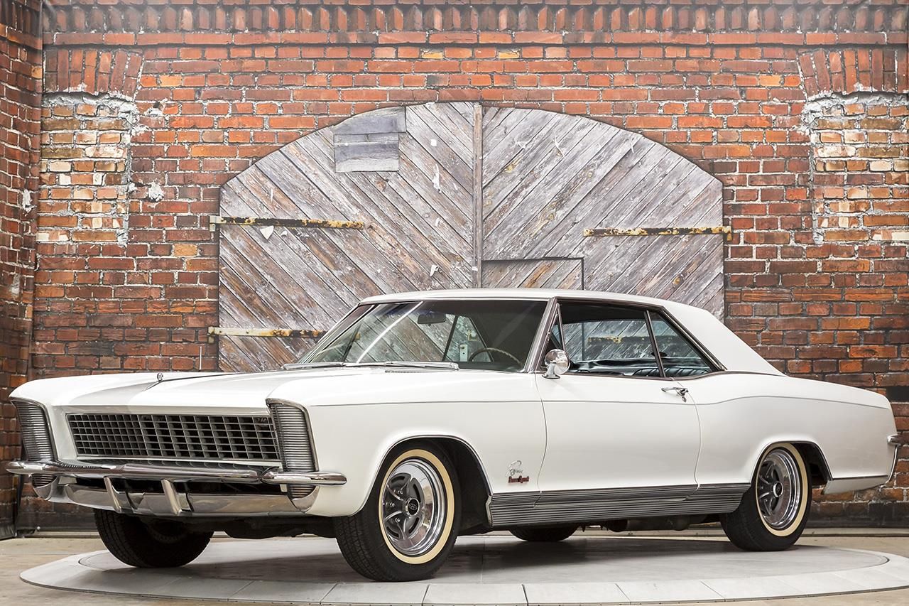 a white 1965 Buick Riviera in front of a brick building