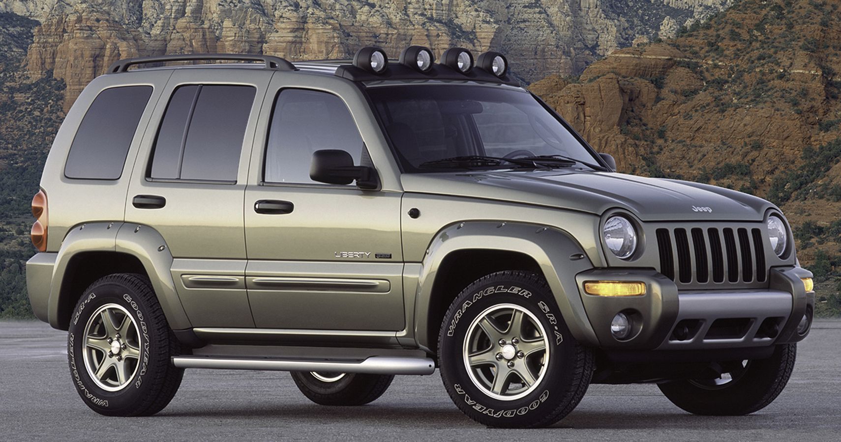 A green 2002 Jeep Liberty is parked at the base of a mountain.