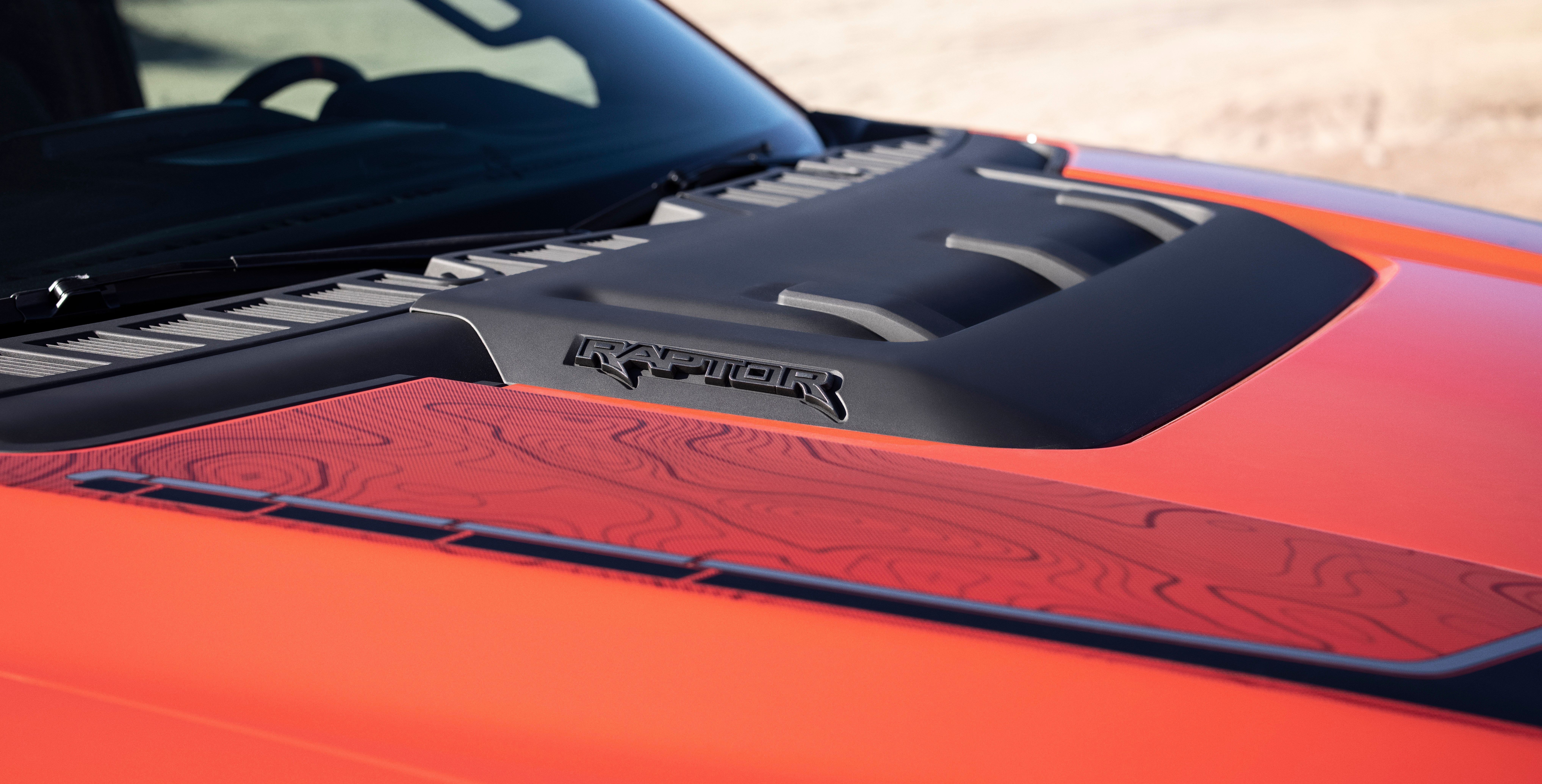 The hood bulge shows Raptor emblazoned on the side of a red 2021 Ford F-150 Raptor pickup