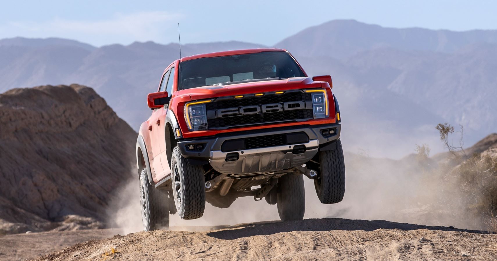 A red 2021 Ford F-150 Raptor jumps a sand dune