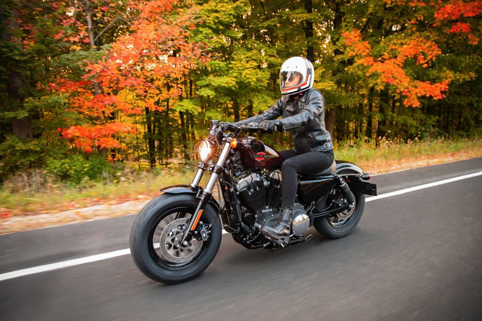 A woman drives the 2021 Harley Davidson Forty-Eight down a road during the autumn season.