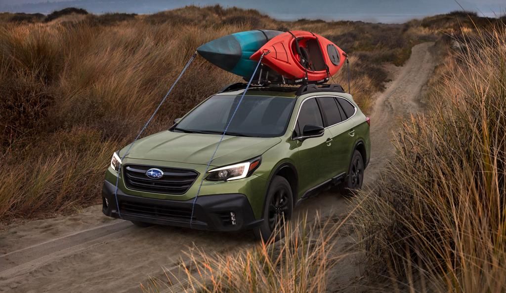green subaru outback 2021 on dirt trail with kayaks on roof
