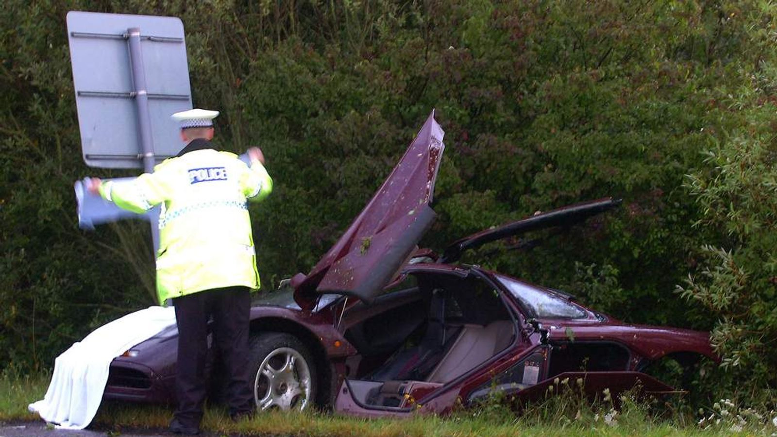 Crashed McLaren F1 in ditch with police officer attending scene