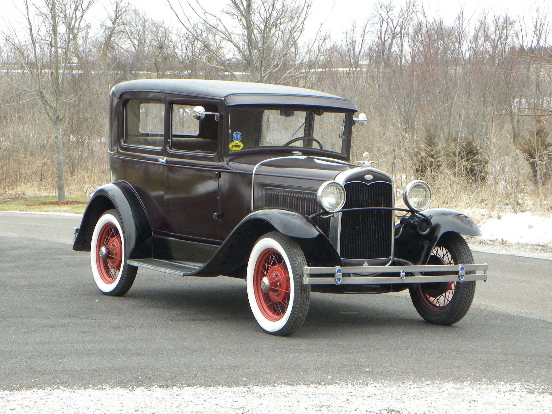 Black Ford Model A on winter road with leafless trees behind it