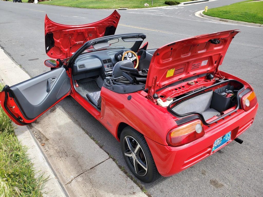 An Image Of A Red Honda Beat With Open Doors
