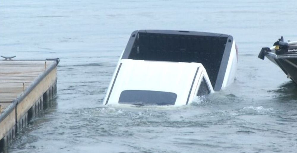White GMC pickup protrudes from lake surface before sinking