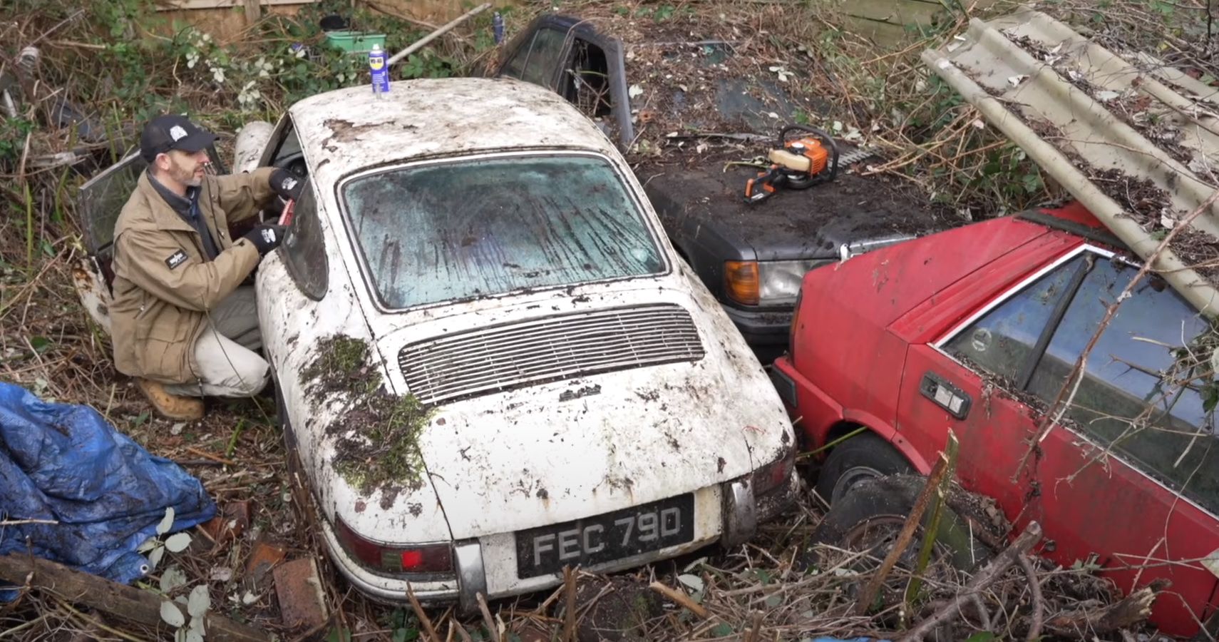 Man examines three abandoned cars in a garden