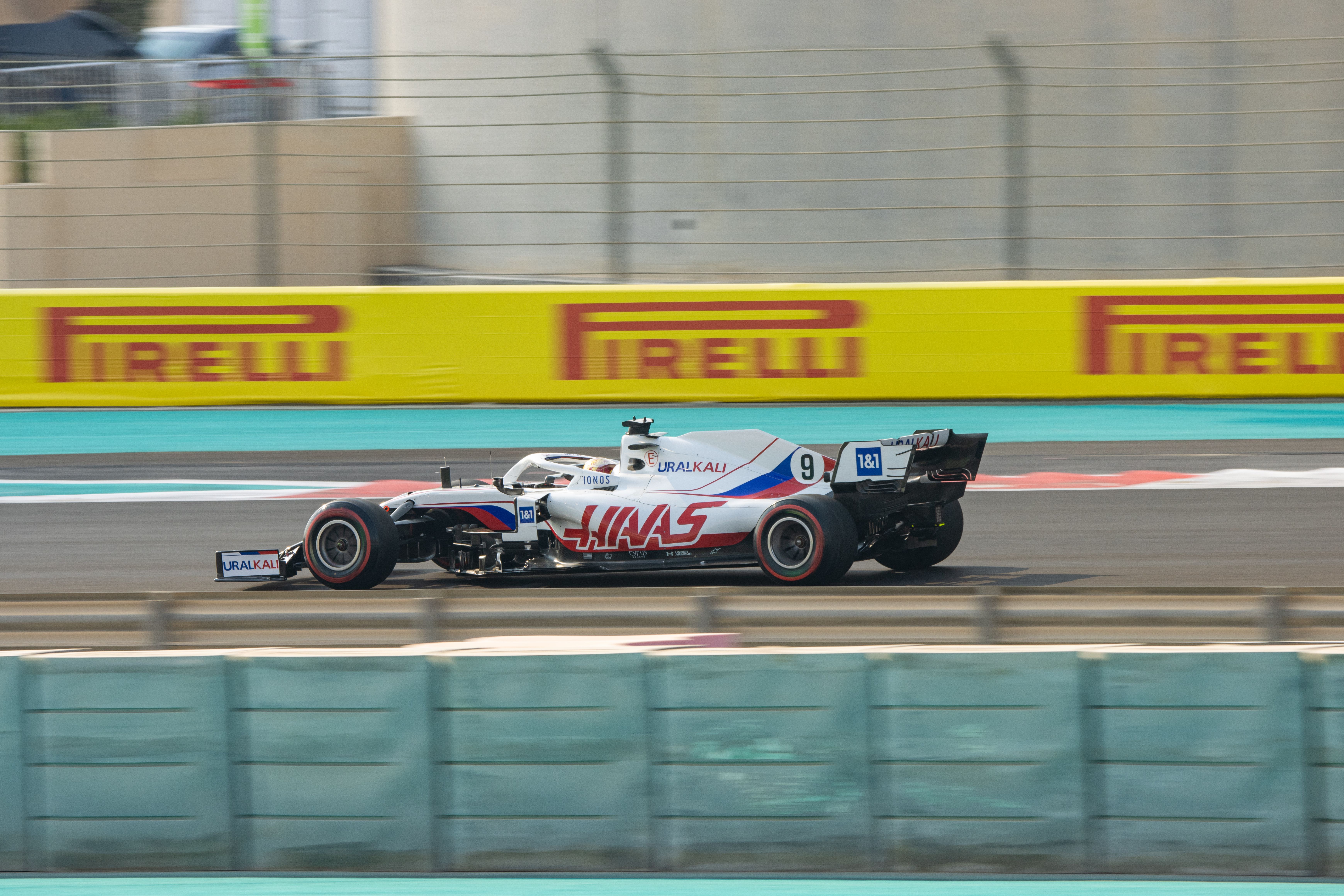 Nikita Mazepin at the Yas Marina Circuit, driving in FP3 for the Formula One finale in Abu Dhabi, 2021. His car is white with a red and blue livery, the team name "Haas" is written down the side. His car sports the number 9.