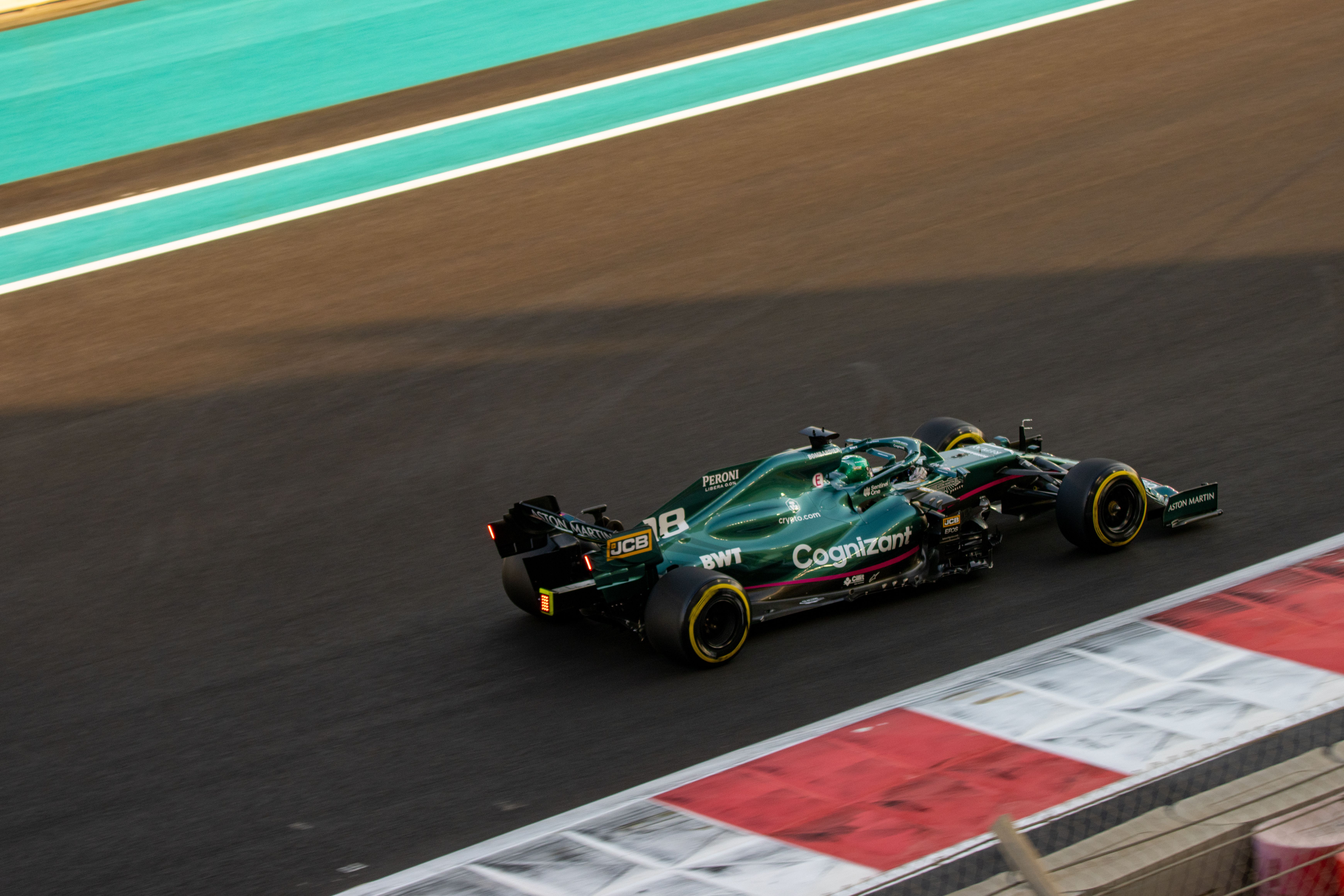 Aston Martin F1 driver Lance Stroll drives past the camera at the 2021 Abu Dhabi Grand Prix. The car is a greenish grey with the number 18 on the side.