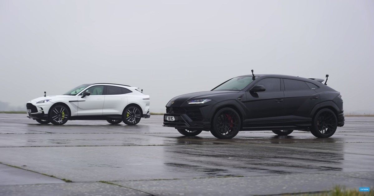 Aston Martin DBX, white vs Lamborghini Urus, black, parked in rain on track
