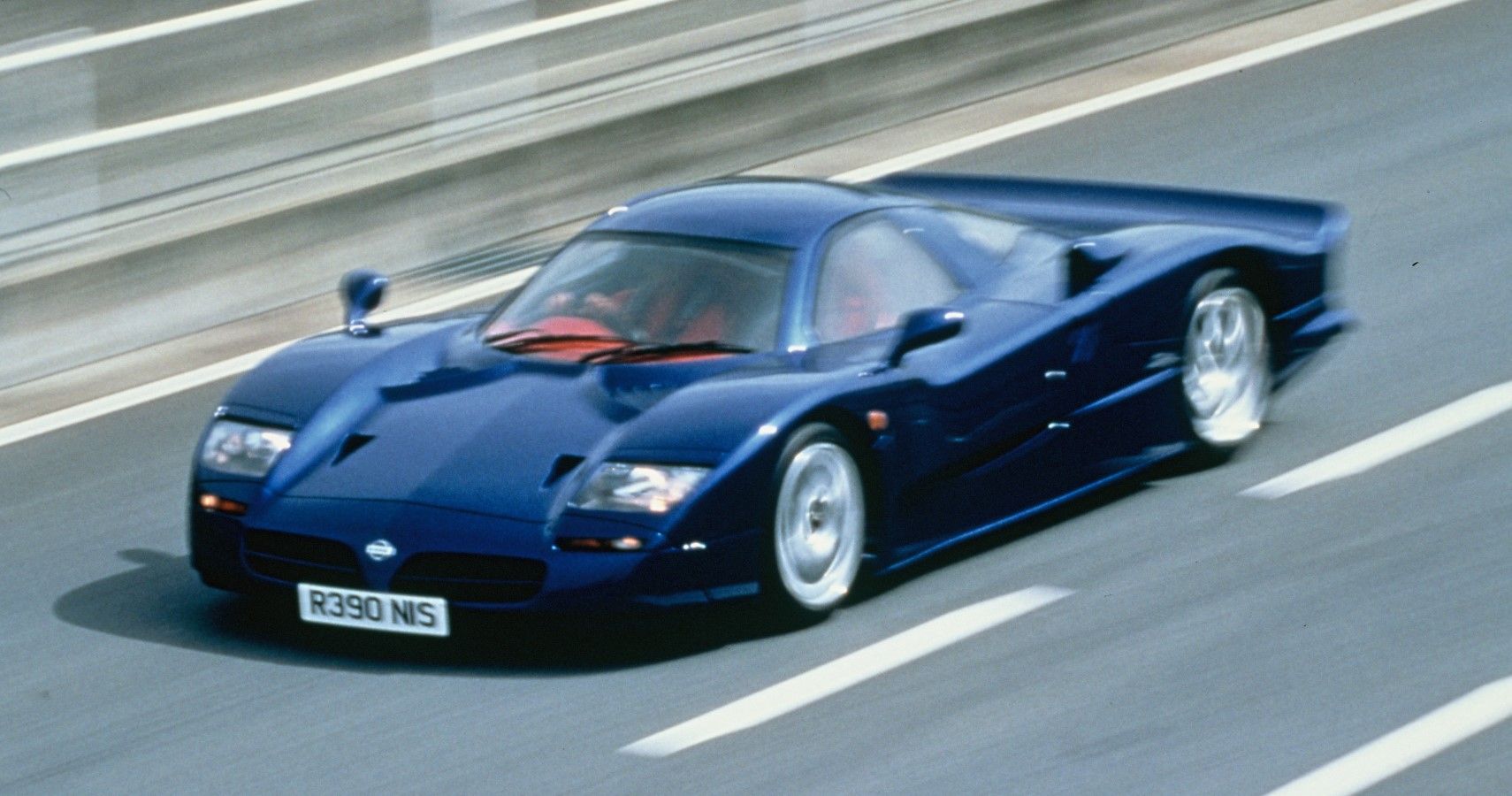 Nissan R390 GT1 accelerating on track front third quarter ariel view