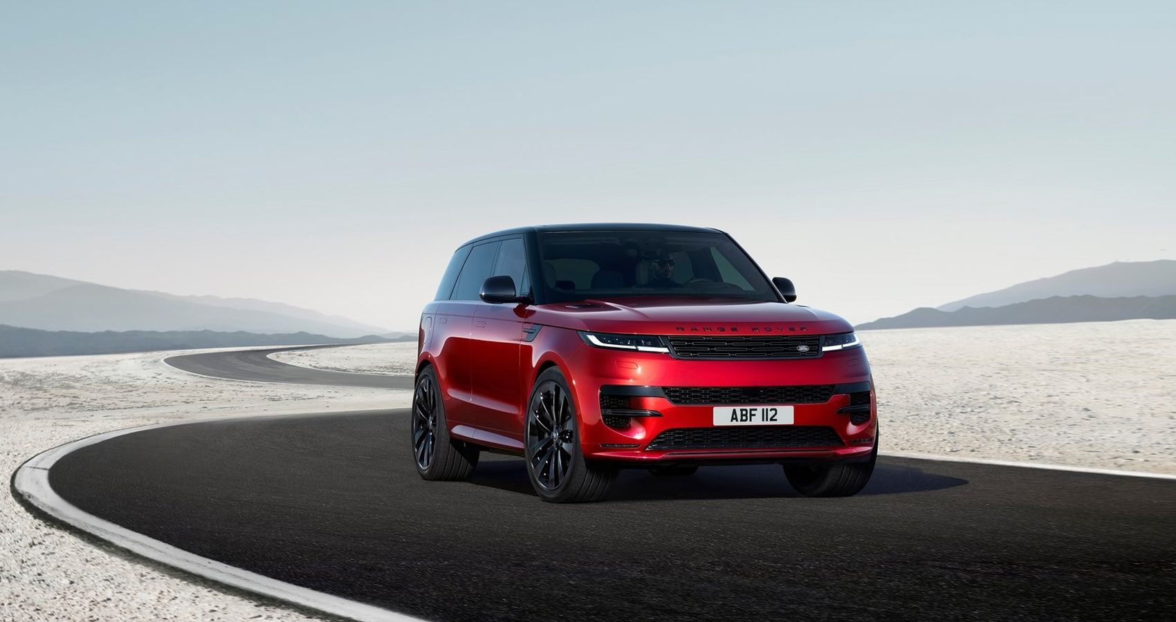 Front 3/4 view of a red 2023 Range Rover Sport, on a desert road 