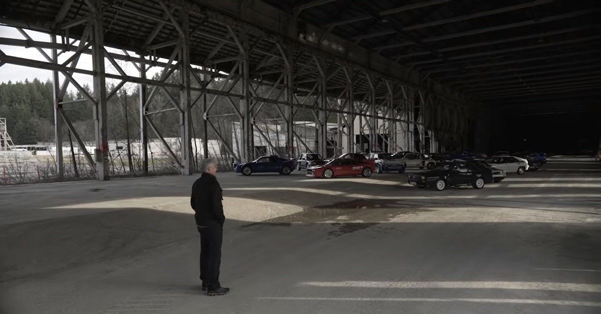 DirtFish rally car collection, cars scattered in hangar in distance with presenter in foreground