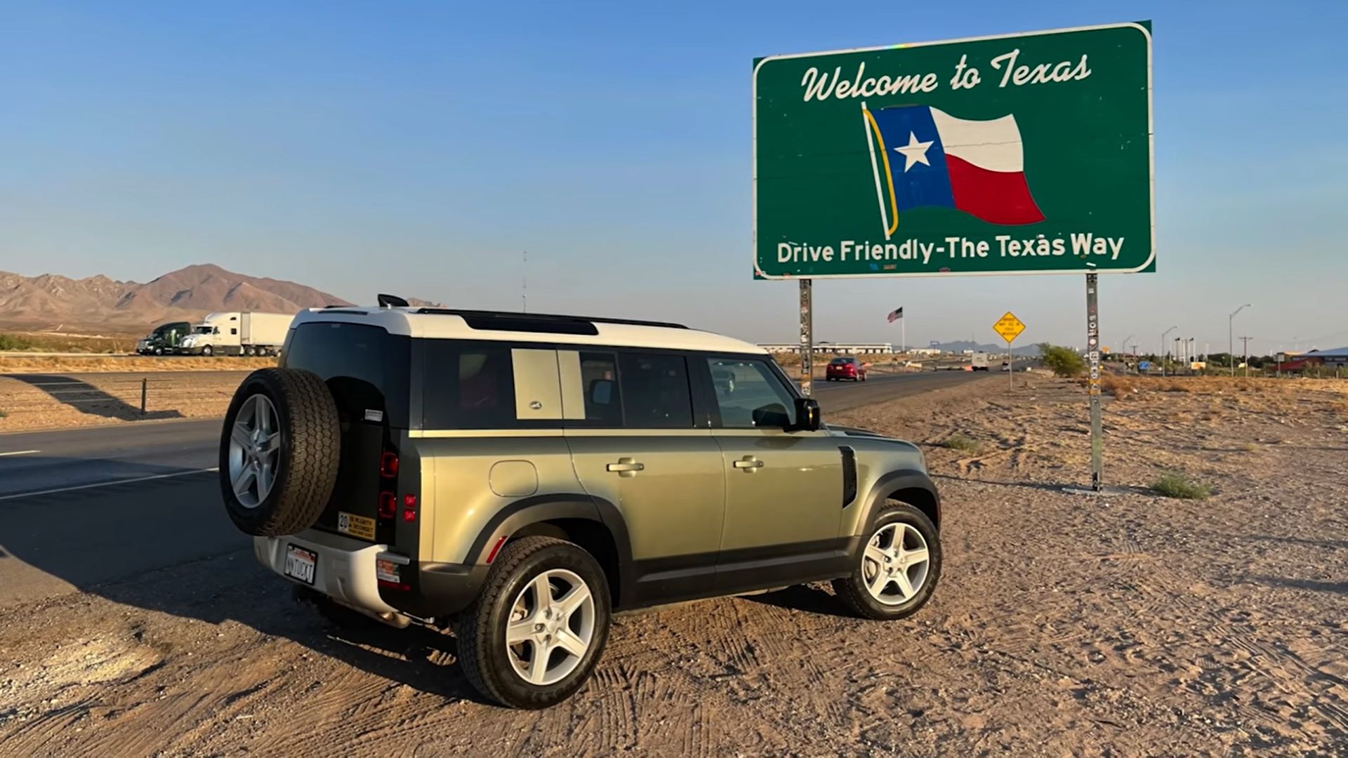 Doug Demuro's Land Rover Defender, mettalic bronze, rear quarter view in desert infront of Texas sign