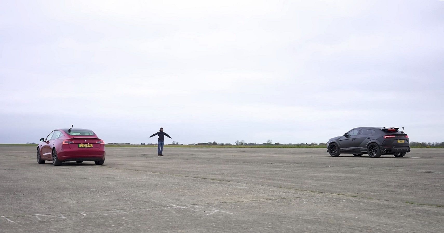 Lamborghini Urus vs Tesla Model 3 drag race, on runway before race, rear quarter view from distance