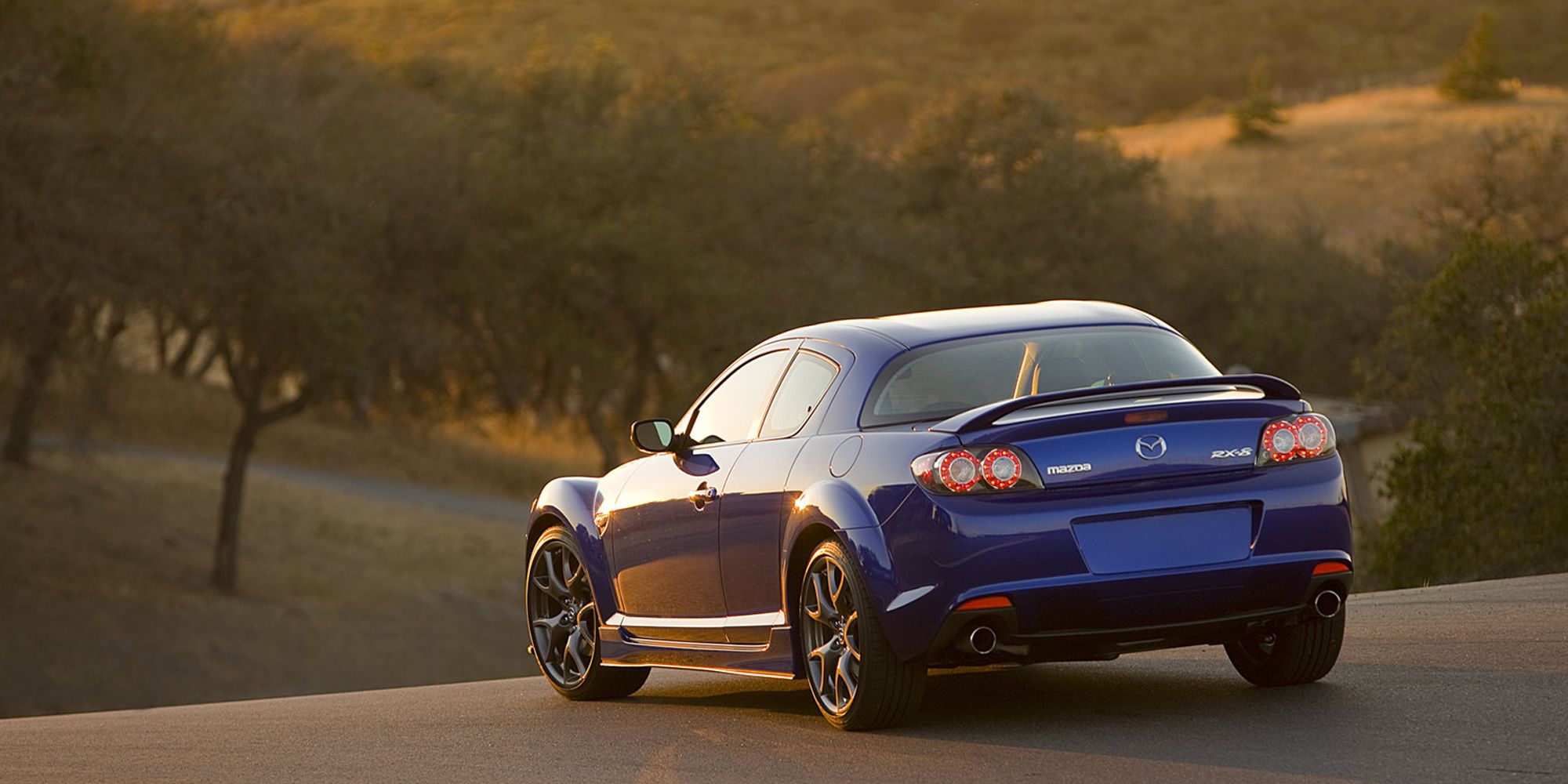 Rear 3/4 view of a blue Mazda RX-8 in the sunset